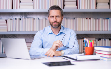 Obraz premium Portrait of teacher in library classroom. Handsome teacher in university library. Teachers Day. Teacher giving classes. School teacher in library. Tutor in classroom at college library.