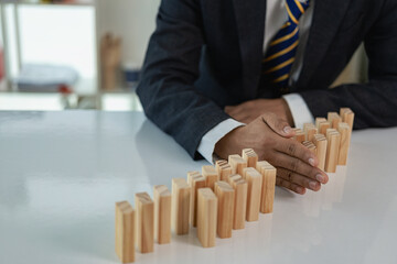 Businessman's hands protecting domino effect from danger and falling, insurance and emergency plan...
