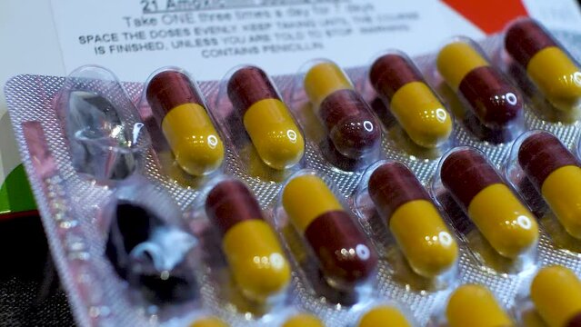 A close-up view of Amoxicillin Capsules as the dark red and yellow components are delicately arranged into their original packaging, and two pills are taken out.