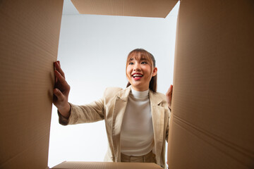 Smiling young woman opening a carton box, relocation and unpacking concept - 729809397