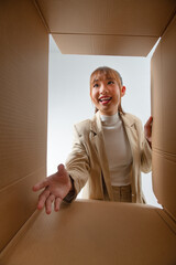 Excited asian woman unpacking, opening carton box and trying to get something, view from the inside