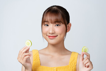 Beautiful young woman with cucumber slices on light background