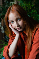 Young red hair woman florist posing at workplace with green potted plants background