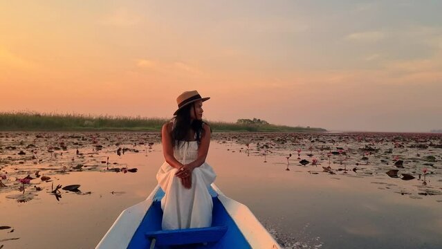 The sea of red lotus, Lake Nong Harn, Udon Thani, Thailand, a Asian woman with a hat in a boat at sunrise at the Red Lotus Lake in the Isaan