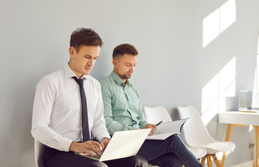 Two business men people sitting on chairs in a row with notepad and laptop. Company employees...