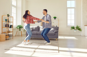 Happy and young couple playful dances and laughing. Movements and smiles create an atmosphere of relax and togetherness. Moment captures the family enjoying each other company in the comfort of home.