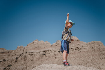 Young boy raising his hand on top of a rock formation of Badlands National Park