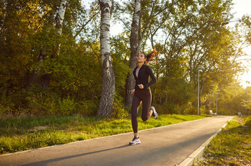 Female young runner jogging alone in city park. Healthy sporty fitness woman running outdoors...
