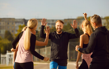 Group of sport people share smiles and exchange high fives during a workout in the park. Image captures the essence of teamwork and community, as each participant contributes to the collective energy.