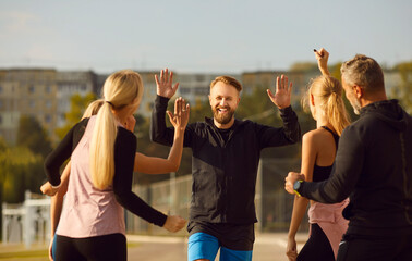 Group of sport people share smiles and exchange high fives during a workout in the park. Image...