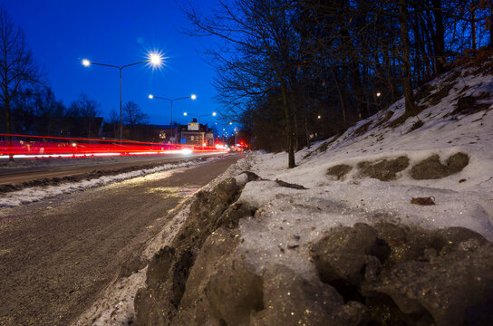 Gray dirty snow next to a path on the side of the road, long exposure photography of traffic at dusk in Västerås, Sweden