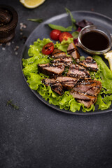 sliced pieces of Organic grilled Tuna Steak on black ceramic serving dish with salad on a table