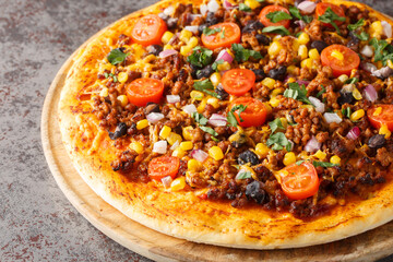 Spicy Mexican Taco pizza with ground beef, tomatoes, corn, black beans, cheddar cheese, red onion on the wooden board on the table. Horizontal