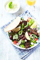 Tasty salad with grilled beef steak, cherry tomatoes and lettuce. White wooden background. Close up.	