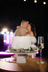 an elegant white wedding cake decorated with a green sprig against the background of a kissing newlywed couple