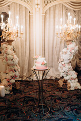 elegant white two-tiered wedding cake decorated with flowers on a small table against the backdrop...