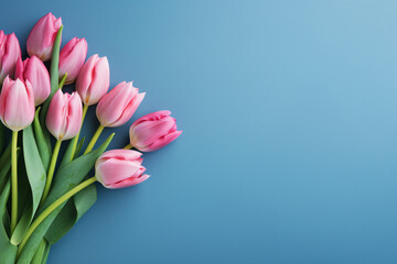 Bunch of pink tulip spring flowers on side of blue background with copy space