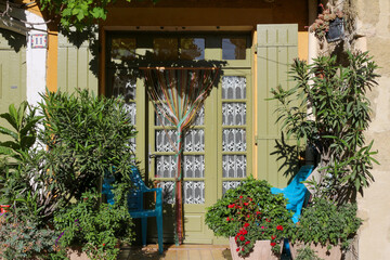 Fototapeta na wymiar Beautiful facade in a French village of Provence called Eyguières, Eyguière, in the south of France. Colored shutters, lush mediterranean vegetation : ivy, oleander, vine creeper.