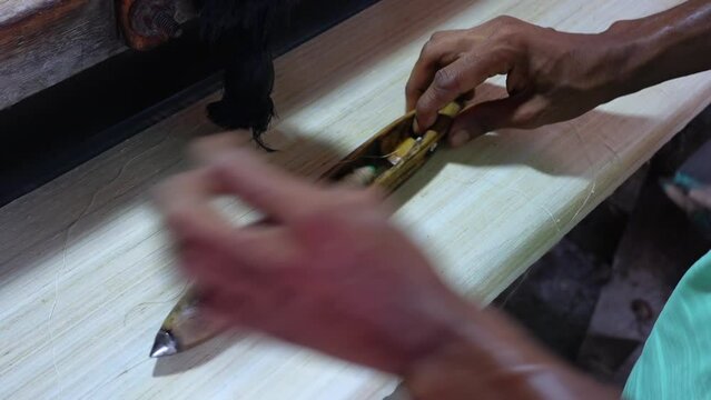 A worker works on a machine using yarn on a wooden boat shuttle to make silk cloth