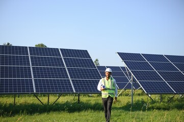 Male arab engineer standing on field with rows of solar panels.
