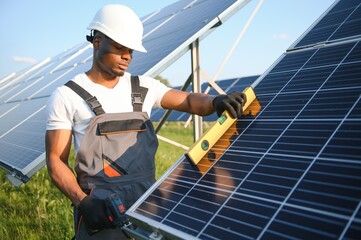 Portrait of african american electrician engineer in safety helmet and uniform installing solar panels.