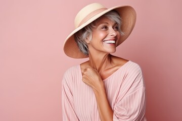 Portrait of happy senior woman in summer hat over pink background.