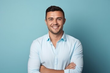 Portrait of a handsome young man smiling with arms crossed over blue background