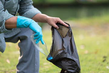 close up volunteer hands picking up plastic bottle and putting garbage bag in the park