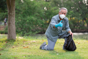 Naklejka na ściany i meble senior man or volunteer wearing face mask holding garbage bag and thumbs up pose in the park