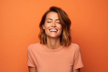 Portrait of a happy young woman laughing with closed eyes on orange background