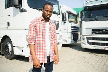 Front view. Young african truck driver is with his vehicle at daytime.