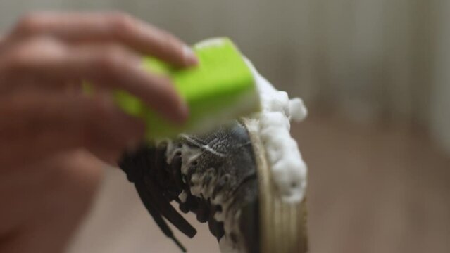 Close-up hands of unrecognizable man washing dirty black shoes using sponge and foam. Repairman wiping sneakers from dirt and dust at workshop. Concept of caring for footwear. Shooting in slow motion.