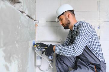Horizontal snapshot of young plumber working with grey sewer pipes, fixing them to wall with a help of screwdriver.