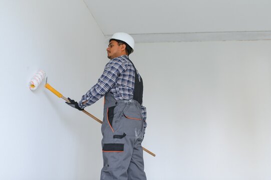 An Indian apartment repair worker paints a white wall with a roller.