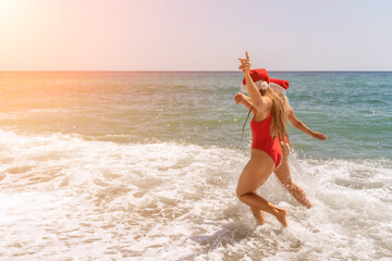 Women in Santa Claus hats run into the sea dressed in red swimsuits. Celebrating the New Year in a...