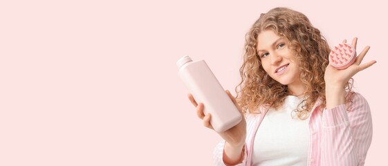 Beautiful young woman with hair scalp massager and shampoo on pink background with space for text