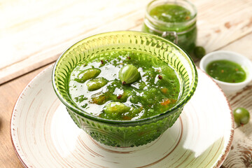 Bowl with tasty gooseberry jam on light wooden background