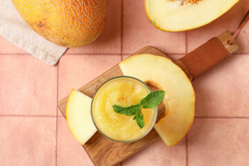 Wooden board with glass of tasty melon smoothie and mint on pink tile table