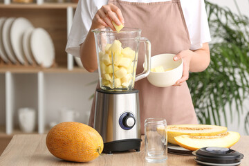 Woman preparing tasty melon smoothie at table in kitchen
