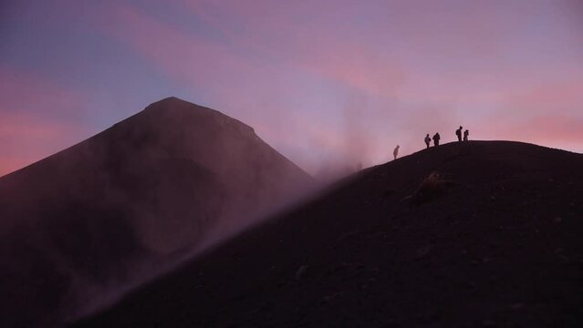 People on ridge of Fuego volcano get hit by dust and strong winds during breathtaking sunset with pink clouds, Guatemala.