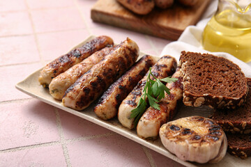 Plate of tasty grilled sausages and bread on pink tile background