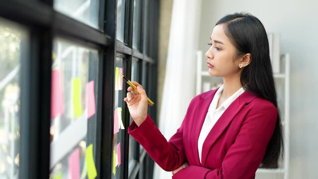 Asian businesswoman using mobile phone with pen to write on notepad business plan idea and find flaws to prevent mistakes in work.