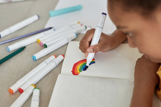 Selective focus close-up of African American kid drawing rainbow with markers in sketchbook