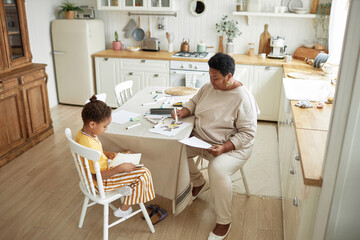 High angle view long shot of modern mature Black woman spending time at home with her granddaughter drawing pictures
