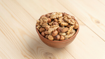 Mixed nuts in a clay cup on a wooden table, walnut kernels, peeled dried hazelnuts, almonds and...
