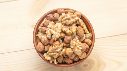 Mixed nuts in a clay cup on a wooden table, walnut kernels, peeled dried hazelnuts, almonds and cashews, top view, healthy and wholesome food concept