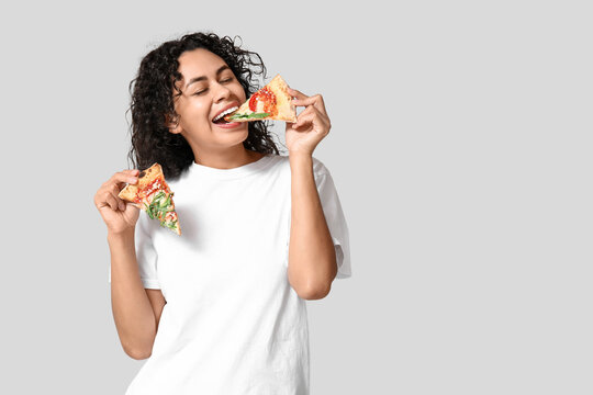 Beautiful young happy African-American woman with slices of delicious pizza on grey background