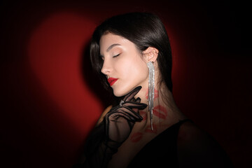Naklejka premium Beautiful woman with lipstick kiss marks on her neck against dark background, closeup