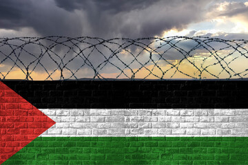 A brick wall with barbed wire in the colors of the national flag of Palestine against a stormy sky....