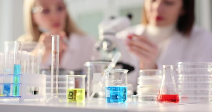 Two scientists working discussing colorful liquid samples in glass flasks together during science experiment on a table